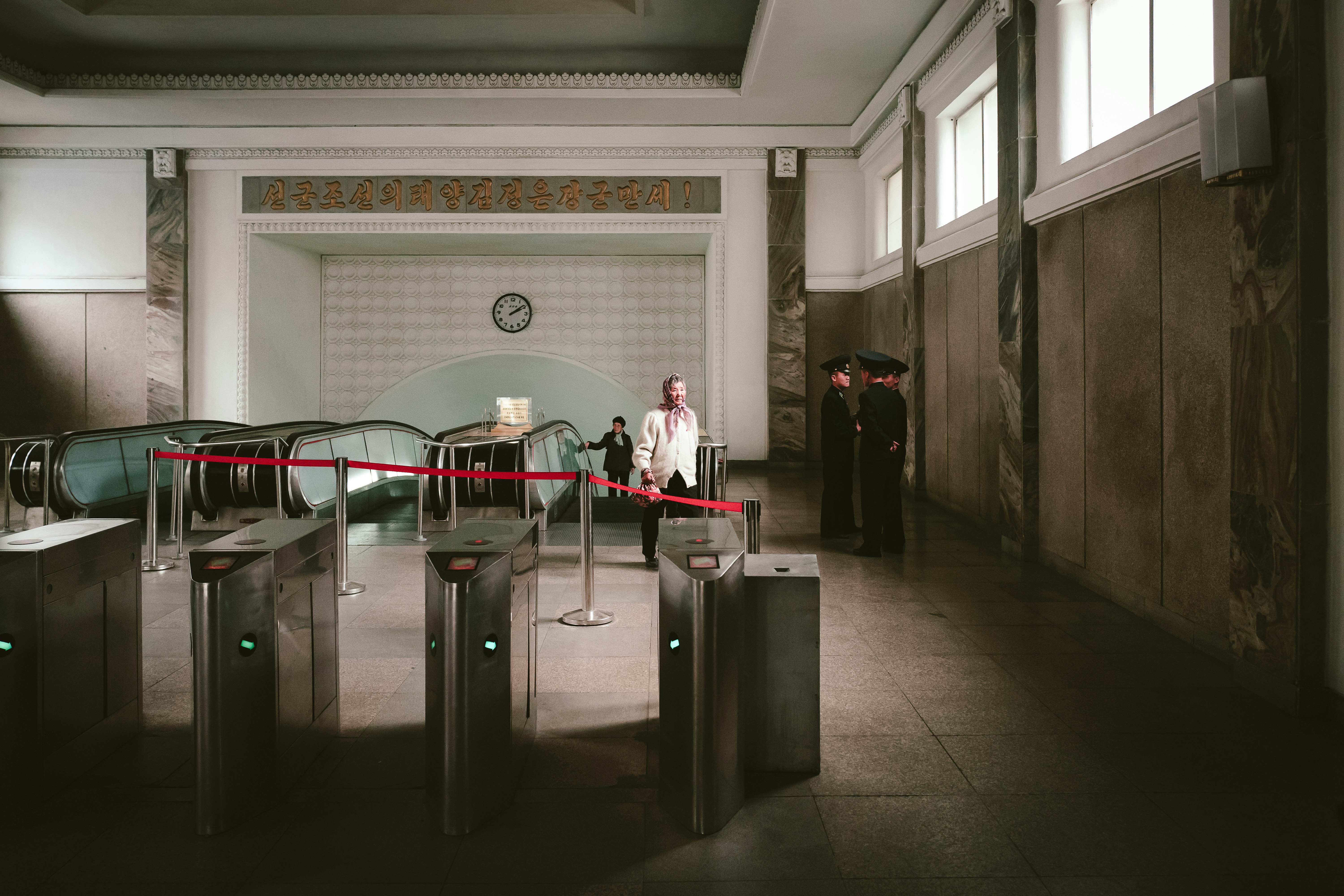 three soldier men standing near pathway and another woman walking going on escalator inside building